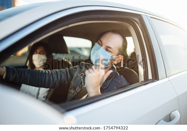 Young man angry drives a car with a passenger\
during coronavirus pandemic. Taxi driver wears a mask sitiing\
behind the steering wheel. Social distance, epidemic, protection,\
health concept.