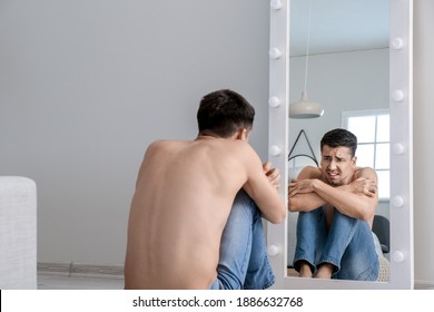 Young Man With Anorexia Looking On His Reflection In Mirror At Home