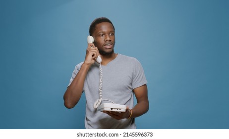 Young Man Answering Landline Phone Call In Studio, Having Remote Conversation On Office Telephone With Cable. Person Having Discussion On Telework Communication Device, With Wired Cord.