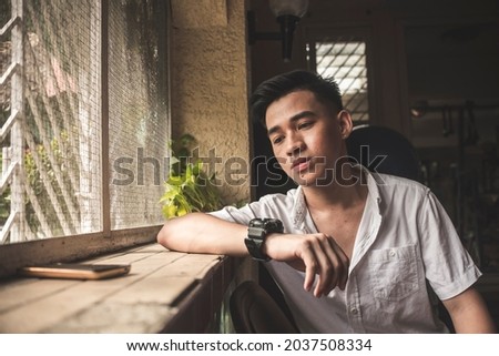 A young man anxiously awaiting a reply from his girlfriend after messaging her multiple times in desperation. Waiting in a dim room.