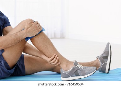 Young Man Applying Cold Compress To Leg At Home