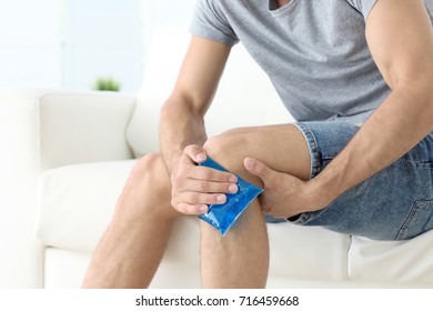 Young Man Applying Cold Compress To Leg At Home