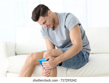 Young Man Applying Cold Compress To Leg At Home