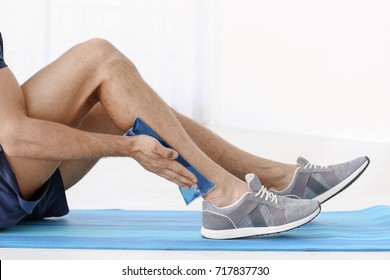 Young Man Applying Cold Compress To Leg At Home