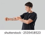 Young man applying cream on his tattooed arm against light background