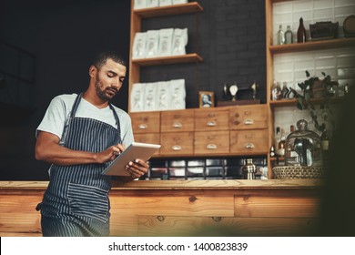 Young man in apron using digital tablet at his cafe