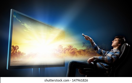 Young Man In Armchair With Click Watching TV