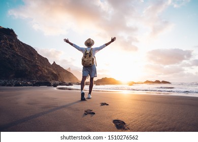 Young man arms outstretched by the sea at sunrise enjoying freedom and life, people travel wellbeing concept