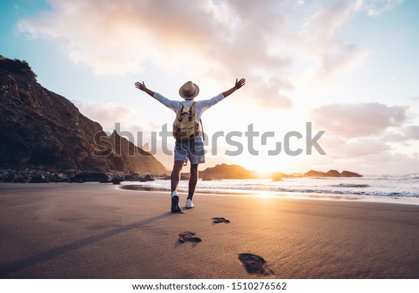 Young man arms\
outstretched by the sea at sunrise enjoying freedom and life,\
people travel wellbeing\
concept