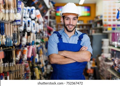 Young Man Artisan With Folded Arms In Paint Store Amongst Racks With Tools