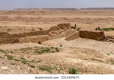 A young man ascends a staircase to nowhere at the ruins of a building, with a sweeping view of an arid landscape in the background. - Shutterstock ID 2311604675