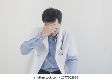 Young man Asian doctor in uniform has stress while sitting on a chair in the white room 
 - Shutterstock ID 1077502988
