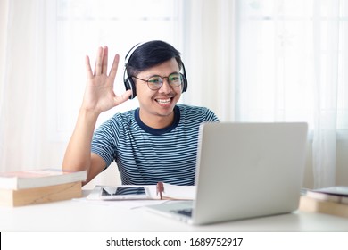 Young Man Asian Having Video Call Via Laptop In His Home Desk. Work From Home Concept