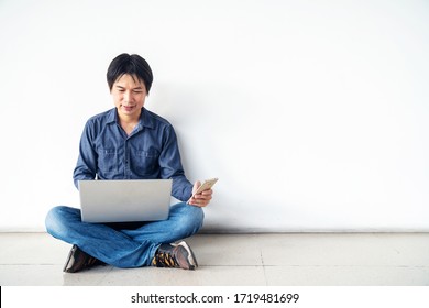 Young Man Asian Sitting On The Floor With Using Computer Laptop And Mobile Phone Is Happy Excited With Big Smile Posing Isolated Over White Wall