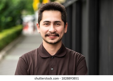 Young Man Asian Smiling And Looking At Camera. Portrait Of A Happy Handsome Young Man In A  Urban Street. Close Up Face Of Young Cool Trendy Man Looking At Camera