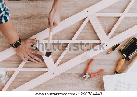 Young Man Assembling Wooden Bookshelf at Home. Wooden Bookcase. Selfmade Furniture. Man and Hobby. White Room. Engineer with Tool. Young Man at Home. Homemade Decoration. Modern Furniture.