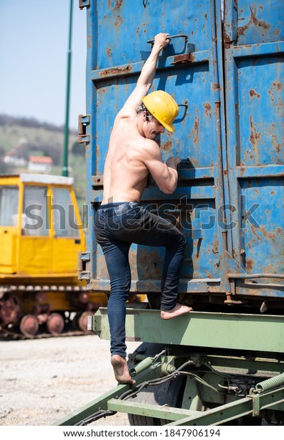 Young Man Athlete is\
Climbing Onto the Trailer Outdoors in Industrial Yard and Wearing\
Yellow Helmet