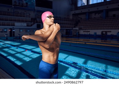 Young man with athletic body, swimmer wearing goggles and pink cap, warming up before swim against blurred background of pool. Concept of aquatic sport, preparation to competition, energy. - Powered by Shutterstock