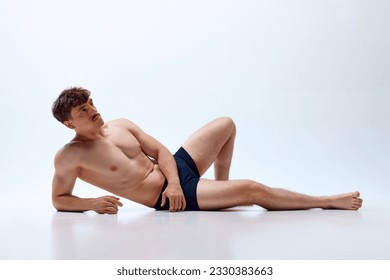 Young man with athletic, muscular, fit body lying on floor, posing shirtless in underwear against white studio background. Concept of man's beauty, sportive and healthy lifestyle, athletic body - Powered by Shutterstock