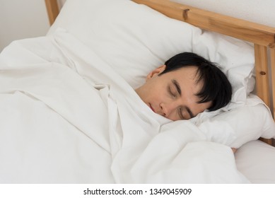 The young man was awakened by the morning alarm clock while on the bed.Shallow depth of field.unhappy from noisy sound of alarm clock and trying to turn it off. Hangover,lazy and sleepless concept.
