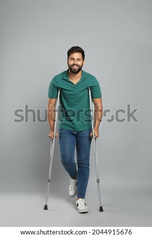 Young man with axillary crutches on grey background