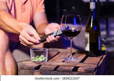 Young Man, Bachelor Sitting On A Couch, Drinking Wine And Eating Unhealthy Snacks, And Watching Movie, Series, Tv Show In The Late Evening, Night.