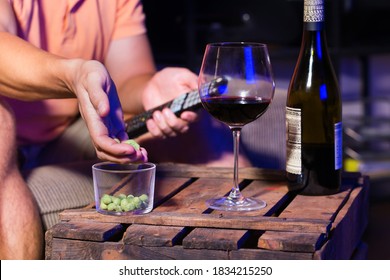 Young Man, Bachelor Sitting On A Couch, Drinking Wine And Eating Unhealthy Snacks, And Watching Movie, Series, Tv Show In The Late Evening, Night.