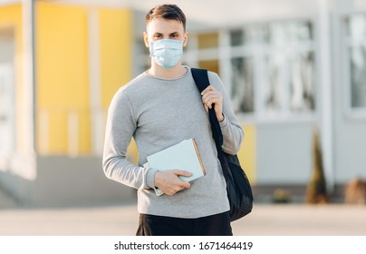 A young man in the background of an open- air building wearing a medical face mask that protects against the spread of coronavirus disease. Close- up of a man with a surgical mask on his face
