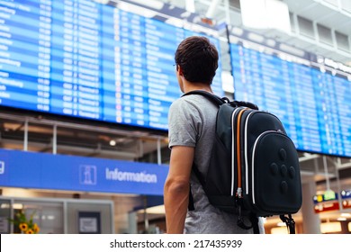 Young Man With Backpack In Airport Near Flight Timetable