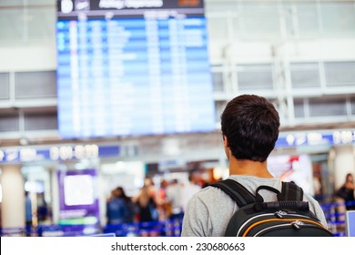 Young Man With Backpack In Airport Near Flight Timetable