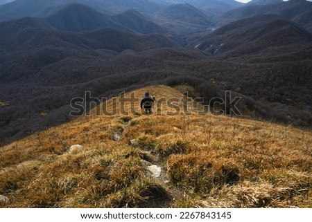 A young man with a backpack descends from the top of the mountain. A man going hiking in the Caucasus mountains. A tourist in the mountains. A young man on top of a mountain enjoying nature. 