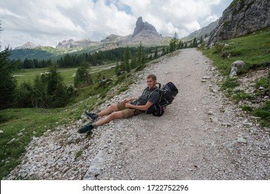 The Young Man With The Backpack Fell Over On The Trail And Sits On A Stone.