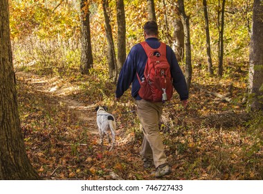 Young Man With A Backpack Hiking Through The Woods With A Dog; Fall In Missouri, Midwest