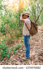 Young man with backpack and holding a binoculars looking forest