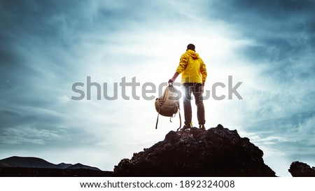 Young man with backpack standing on the top of a mountain at sunset - Goals and achievements