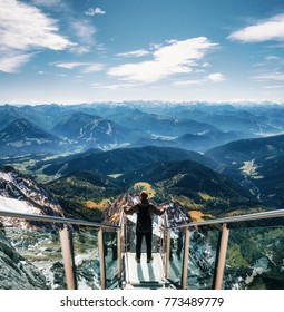 Young man with backpack stands on observation deck of skywalk rope bridge Dachstein Mountains and enjoys the landscape in Austria