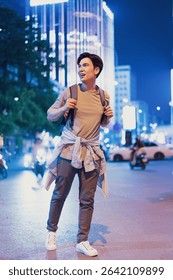A young man with a backpack strolls through vibrant downtown Hanoi at night, illuminated by bright lights and surrounded by busy streets and vehicles.
