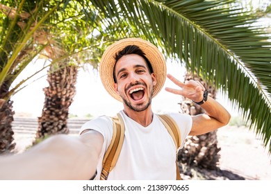 Young Man With Backpack Taking Selfie Portrait On Exotic Beach -Smiling Happy Guy Enjoying Summer Holidays - Millennial Showing Victory Hands Symbol To The Camera