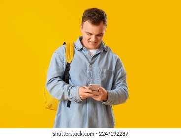 Young man with backpack using mobile phone on yellow background