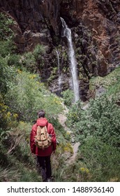 Young man with backpack walking down the mountain towards a waterfall