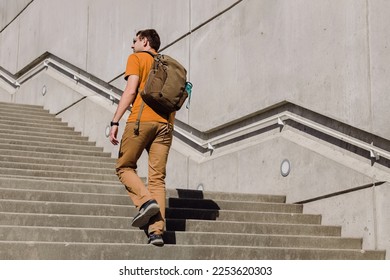 Young man with a backpack walking, going up the stairs in the city. Urban lifestyle