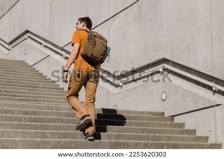 Young man with a backpack walking, going up the stairs in the city. Urban lifestyle