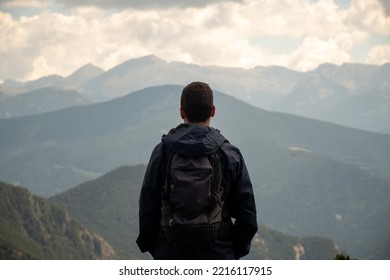 Young Man With A Backpack Is Wearing A Dark Raincoat And He's Enjoying An Amazing Mountain Views In Andorra.