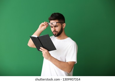 Young Man With Bad Sight Reading Book On Color Background