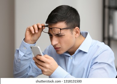 Young Man With Bad Sight Trying To Read Message On Screen Of Mobile Phone