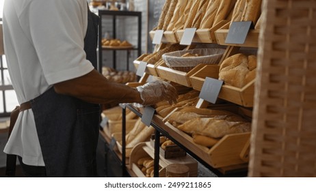 Young man in bakery arranging fresh bread on shelves wearing apron and gloves shop background indoors. - Powered by Shutterstock