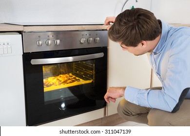 Young Man Baking Bread In Oven Appliance At Home