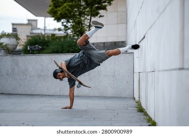 Young man balancing upside down on one hand with a skateboard by his side, showing agility and precision in urban setting
