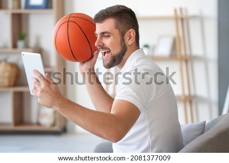 Young man with ball and tablet computer placing sports bet at home