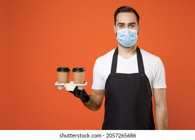 Young Man Barista Barman Employee In Apron White T-shirt Sterile Face Mask Coronavirus Covid19 Pandemic Quarantine Work Coffee Shop Hold Delivery Cups Isolated On Orange Background Business Startup